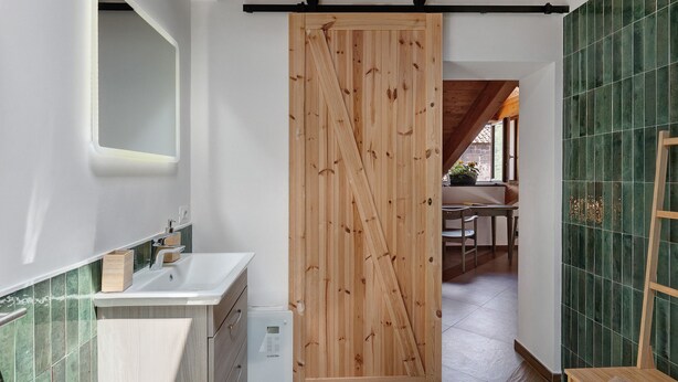Une salle de bain avec une porte coulissante en bois, un lavabo blanc et des murs recouverts de carreaux verts.