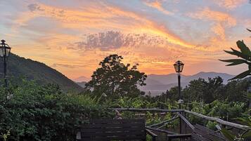 A wooden bench and table set on a patio with a view of a sunset over a mountainous landscape.