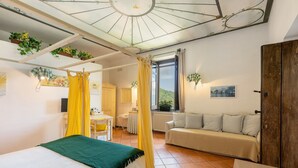 Una habitación con cama, sofá, ventana con cortinas, radiador y ventilador de techo.