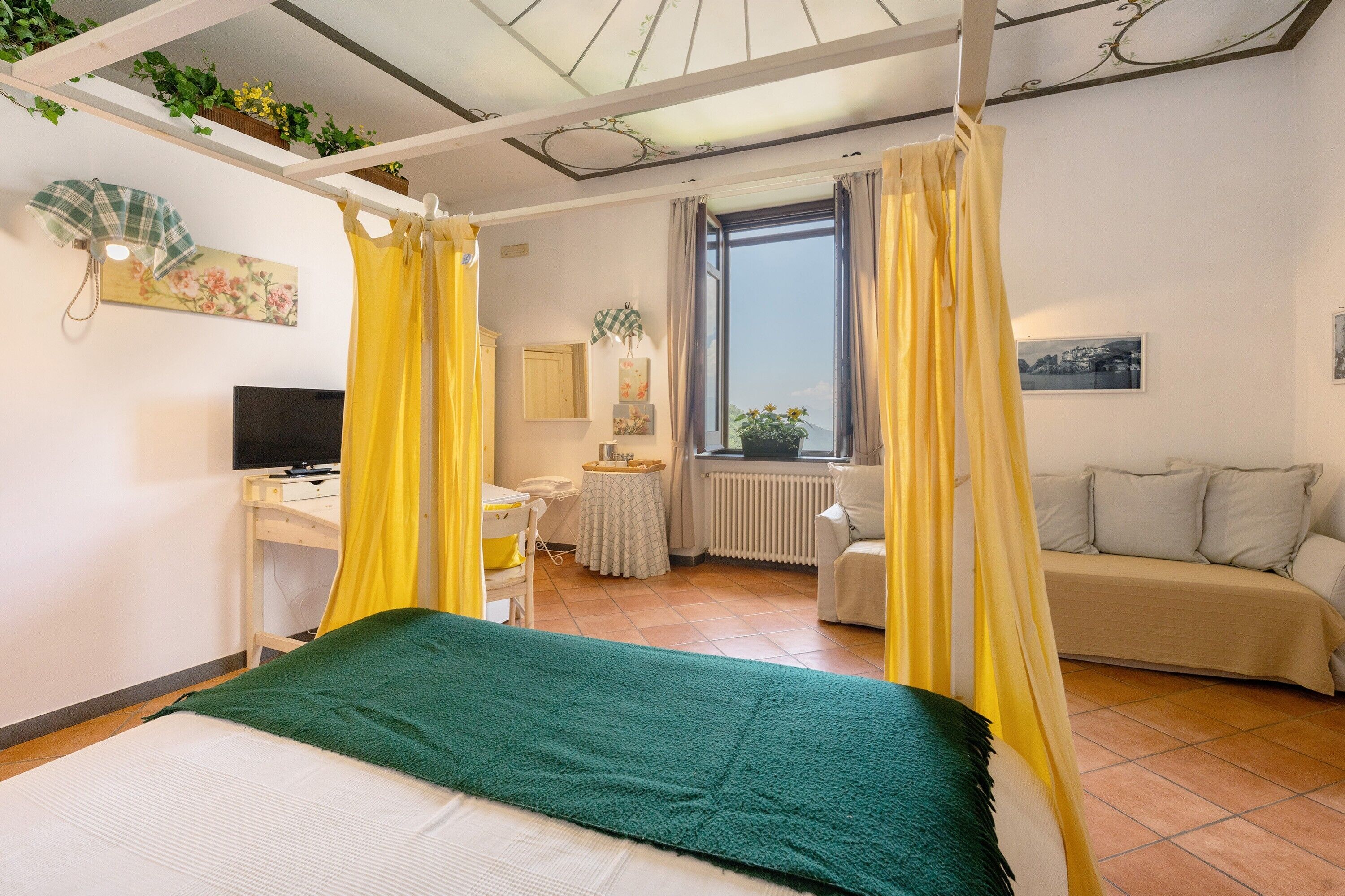 Ein Schlafzimmer mit Bett, Schreibtisch, Stuhl, Fernseher, einem Fenster mit Vorhängen und einer Heizung.