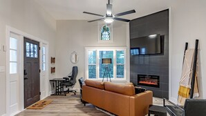 A modern living room with a fireplace, a large window, and a ceiling fan.
