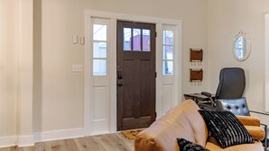 A room with a wooden door, a leather sofa with cushions, a small table, and a mirror on the wall.