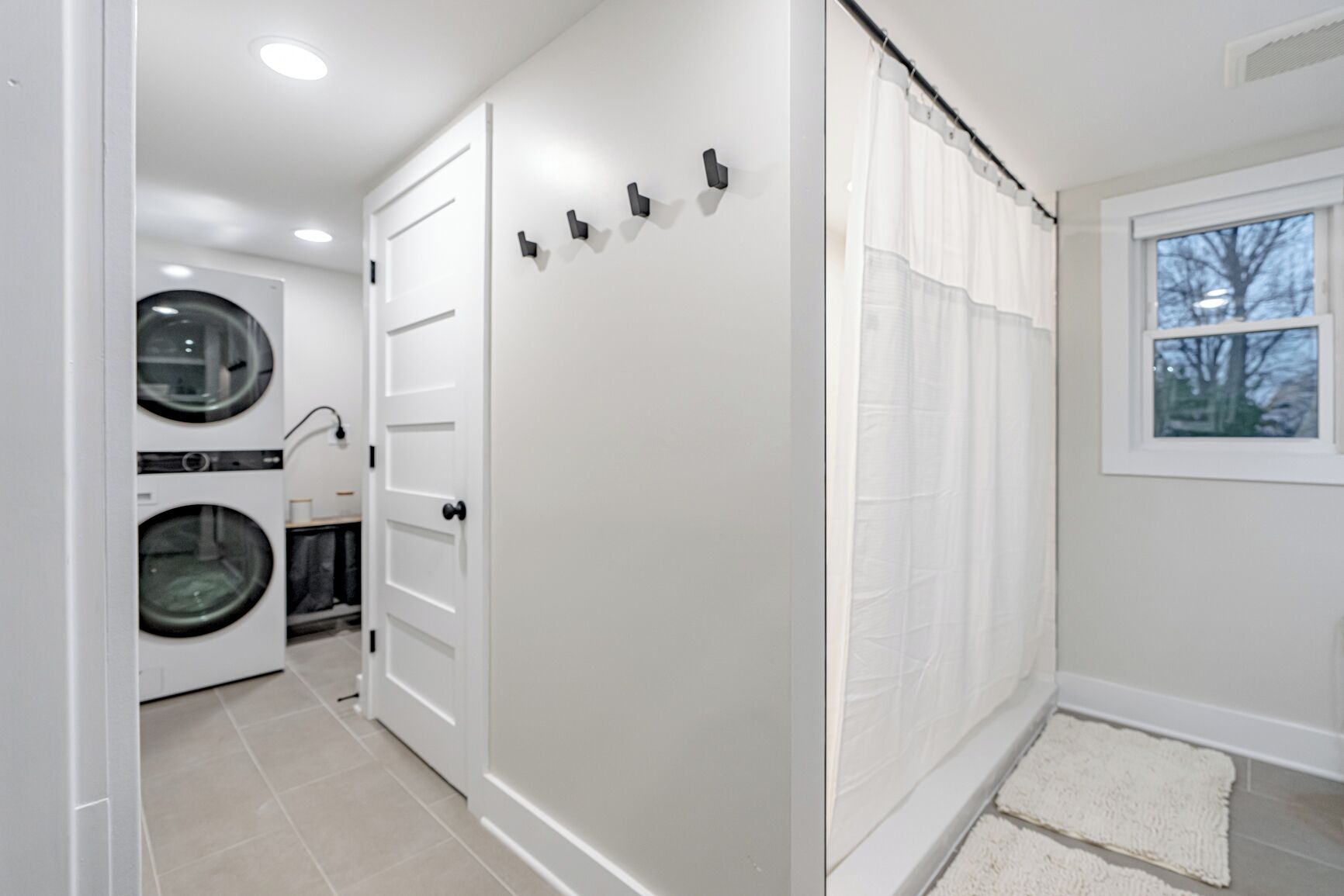 A laundry room with a washing machine, dryer, and a door leading to a shower area with a window.