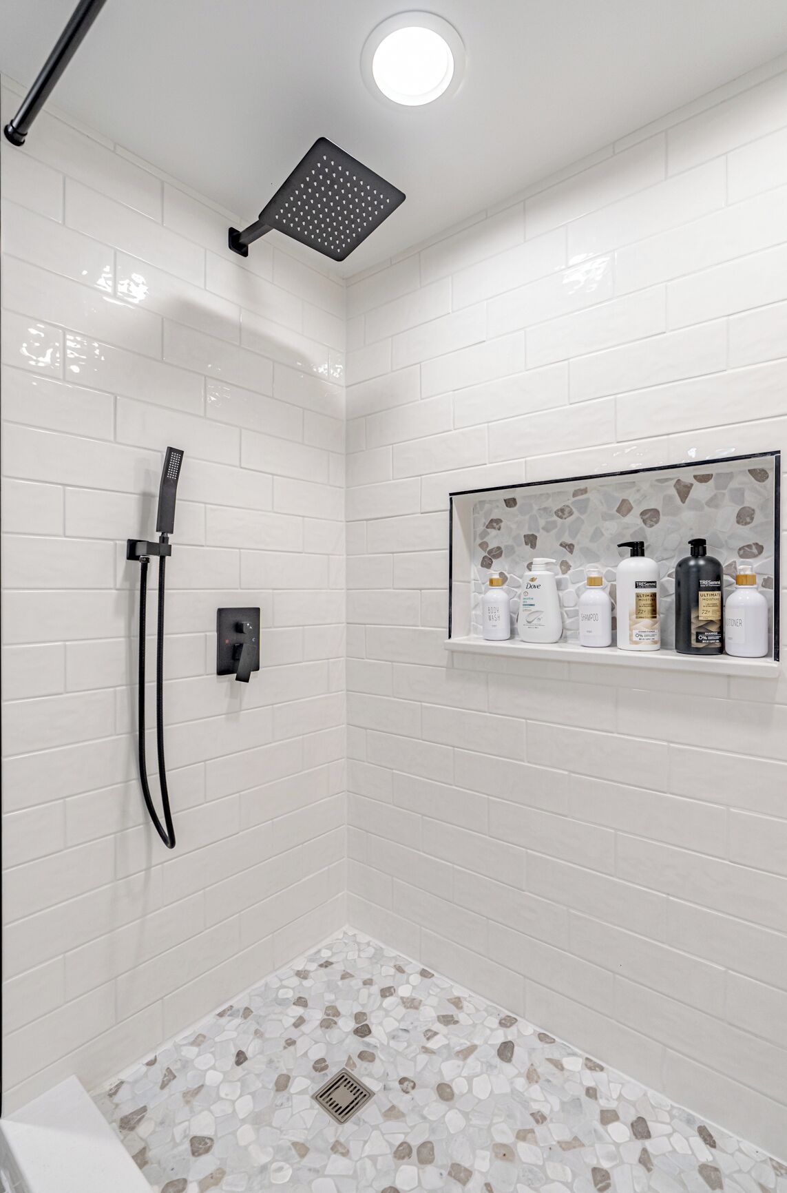 Een douchegedeelte met een handdouche, een bedieningspaneel aan de muur en een plankje met toiletartikelen.