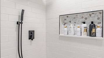 Een douchegedeelte met een handdouche, een bedieningspaneel aan de muur en een plankje met toiletartikelen.