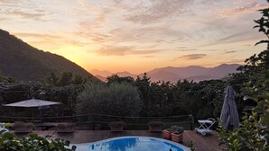 A swimming pool surrounded by greenery, with a view of distant mountains and a sunset.
