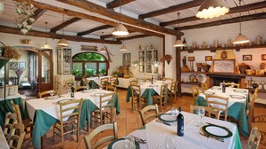 A restaurant with wooden beams, tables set with green tablecloths, and hanging pendant lights.