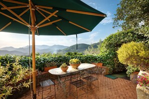 Un patio con mesa y sillas, rodeado de plantas en macetas y vistas a montañas distantes.