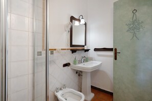 A bathroom with a shower, bidet, sink, mirror, and towel rack.