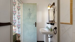 Een badkamer met een wastafel, spiegel en een deur naar een kamer met bloemenbehang.