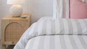 A bedroom with a striped bed, a bedside lamp, a small wooden nightstand, a framed picture, and a hanging plant. - Sunsets ~ Rooftop, Incredible views, 4 KING rooms (Aldinga Beach)