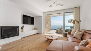 A modern living room with a fireplace, a flat-screen TV, a leather sofa, and a view of the sea through large glass doors. - Sunsets ~ Rooftop, Incredible views, 4 KING rooms (Aldinga Beach)