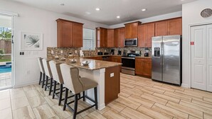 Una cocina moderna con una isla central, armarios de madera, electrodomésticos de acero inoxidable y una piscina visible a través del ventanal.