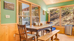 Un tavolo da pranzo in legno con sedie, ampie finestre e vista sugli alberi.