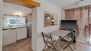 A modern kitchen with white cabinets, a wooden ceiling beam, a dining table with chairs, a TV, and a window with curtains. - Escape to Les Pouges – Renovated House with Garden, Fast Wi-Fi, Barbecue (Saint Avit Saint Nazaire)