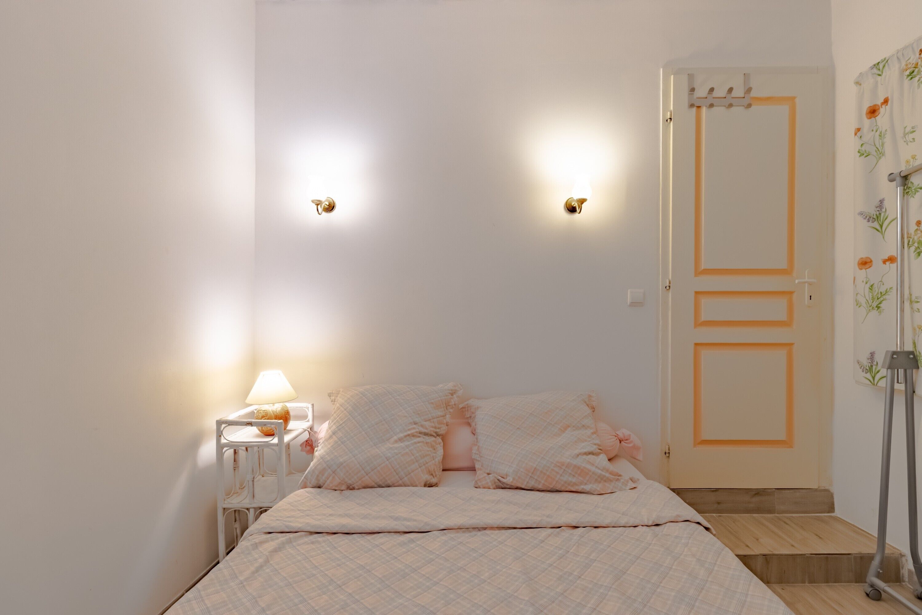 Un dormitorio con cama, mesita de noche, lámpara y una puerta con perchero.