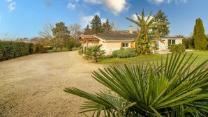 A house with a gravel driveway, a covered porch, and a well-maintained lawn with various plants. - Escape to Les Pouges – Renovated House with Garden, Fast Wi-Fi, Barbecue (Saint Avit Saint Nazaire)