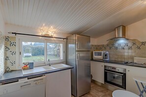 A modern kitchen with a stainless steel refrigerator, a built-in oven, a microwave, and a window with a view of greenery. - Getaway at Les Pouges – Renovated House with Garden, Fast Wi-Fi, Barbecue (Saint Avit Saint Nazaire)