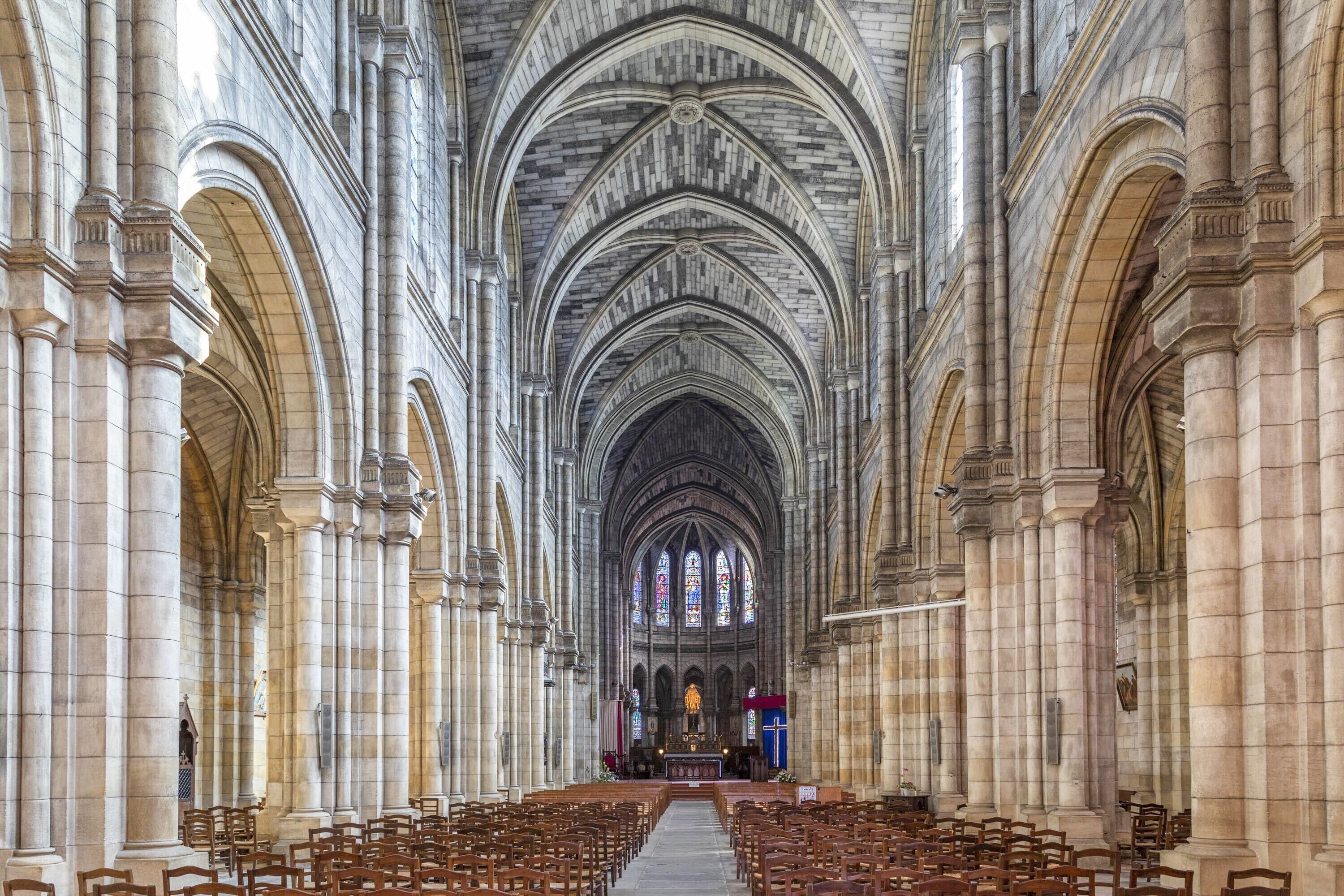 L’intérieur d’une cathédrale, avec de hauts plafonds en voûte, des rangées de bancs en bois et un autel central.