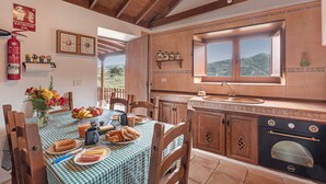 Una cuina amb armaris de fusta, una placa de cocció, un rentataps i una finestra amb vista a un paisatge de muntanya.