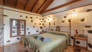 Habitació amb un llit, un sostre de fusta, una paret de pedra, una finestra i una taula de nit amb una làmpada.