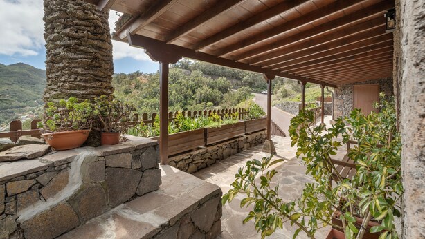 Zona exterior coberta amb parets de pedra, bancs de fusta i plantes en testos.