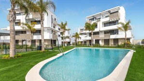 A modern residential building with a swimming pool surrounded by well-maintained grass and palm trees.