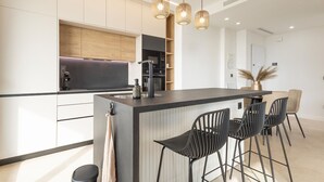 A modern kitchen with a central island, black bar stools, and pendant lighting.