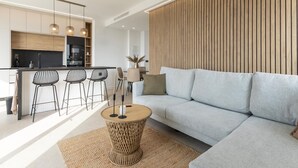 A modern living room with a grey sofa, a small round wooden coffee table, and a kitchen area with a black countertop and wooden cabinets.