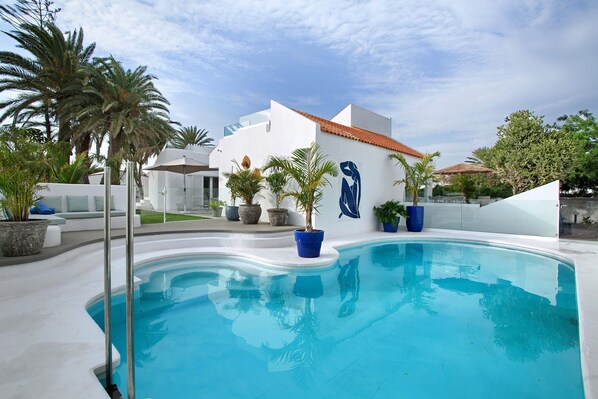 Una piscina con un edificio blanco y palmeras al fondo.