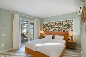 Habitación de hotel con cama, dos mesitas de noche con lámparas, un gran mural floral y una puerta corredera de vidrio que da a un espacio exterior.