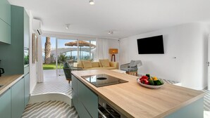 A modern kitchen with a central island, a dining area with a sofa, and a TV mounted on the wall.