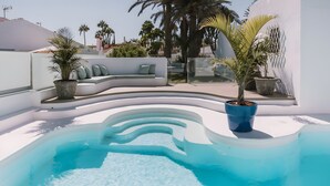 A swimming pool with a white deck, a curved seating area, and potted plants.