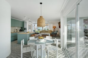 A modern kitchen with teal cabinets, a dining area with a glass table, and a living room with a sofa and coffee table. - Sierra Del Mar – 12 Guests, Sea View, Private Pool, Wi-Fi (Playa del Ingles)