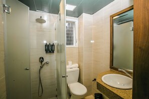 Un baño con ducha de vidrio, inodoro, lavabo con espejo y artículos de aseo en el mostrador.