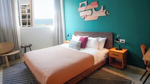 A hotel room with a bed, bedside tables, a chair, a window with curtains, and a wall-mounted abstract art piece. - Domus Tlv (Tel Aviv)