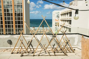 Un balcon donnant sur la mer, des baguettes de bois disposées en motif décoratif et un immeuble doté de balcons.