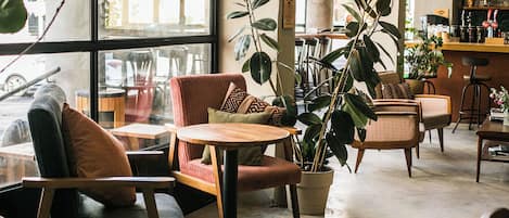 Un acogedor interior de cafetería con asientos cómodos, ventanas amplias y plantas de interior.