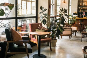 A cozy cafe interior with comfortable seating, large windows, and indoor plants. - Domus Tlv (Tel Aviv)
