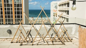A balcony with a view of the sea, wooden sticks arranged in a pattern, and a building with balconies. - Domus Tlv (Tel Aviv)