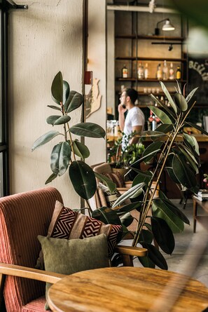 A cozy seating area with a wooden table and a cushioned chair, surrounded by green plants. - Domus Tlv (Tel Aviv)