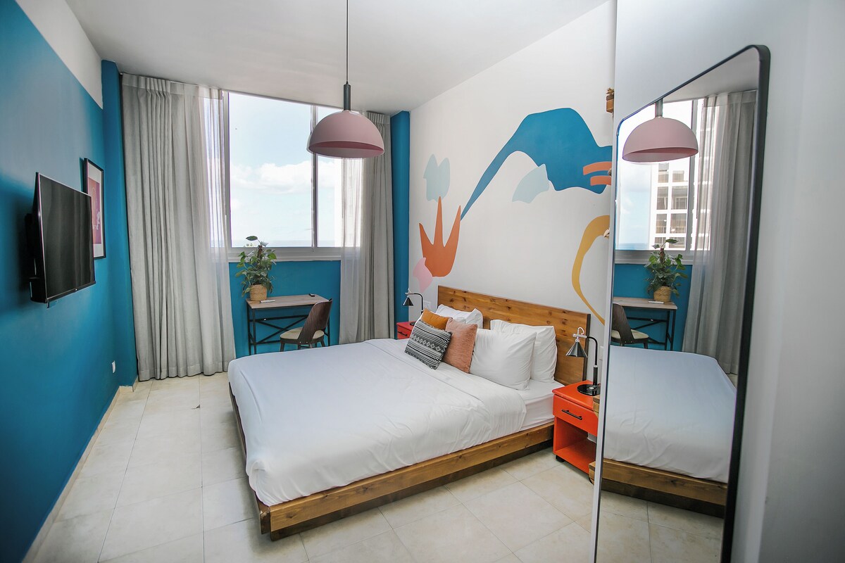 A modern bedroom with a large bed, a desk, and a chair.