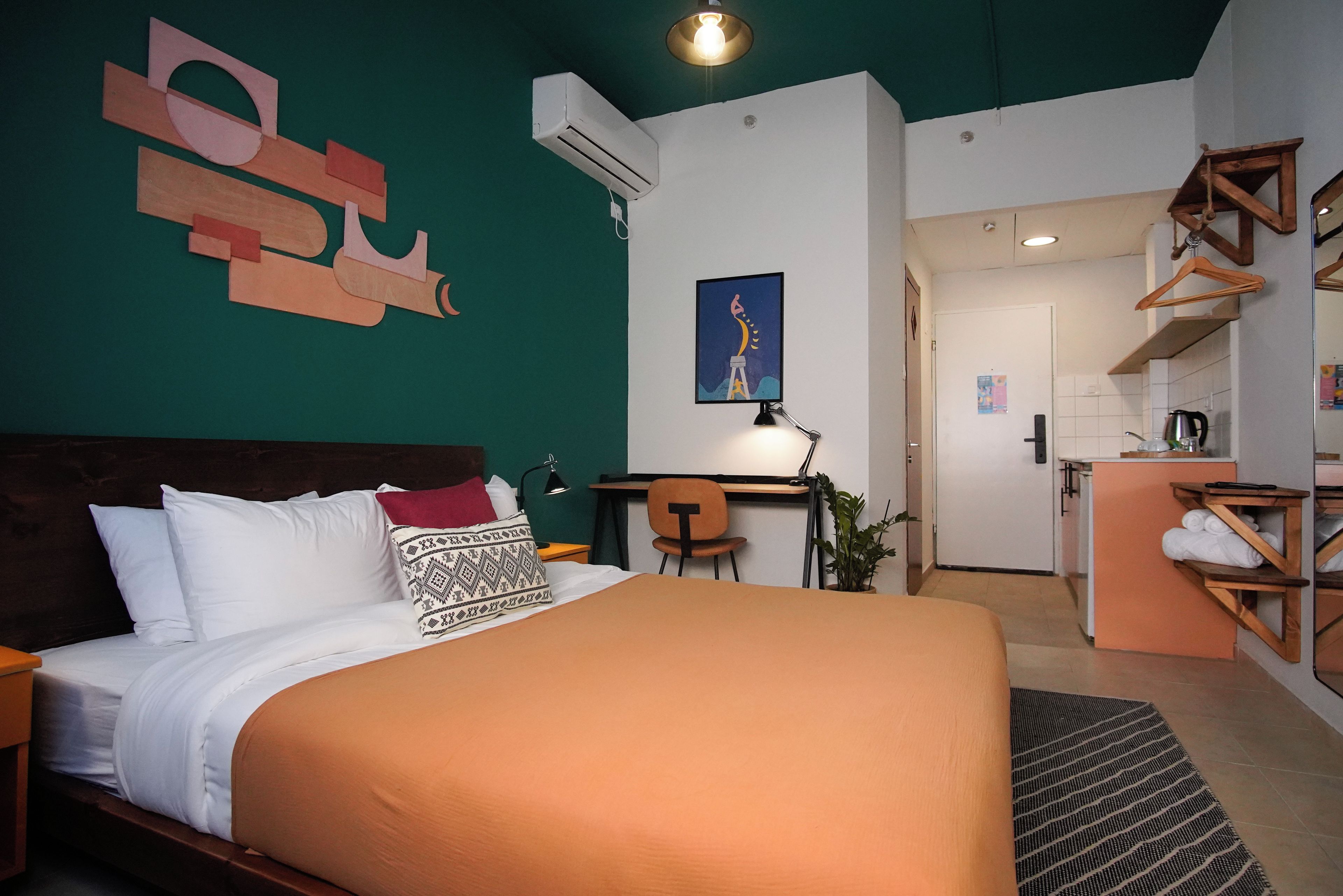A hotel room with a large bed, a desk, a chair, and a kitchenette.