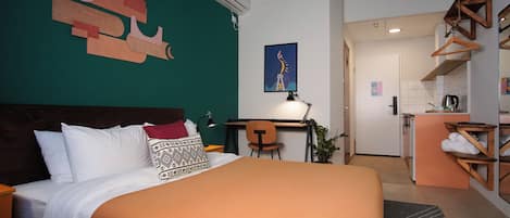 A hotel room with a large bed, a desk, a chair, and a kitchenette.