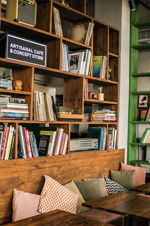 Une bibliothèque en bois remplie de livres, avec une enseigne indiquant : « Café d’artisans et boutique de créateurs ».