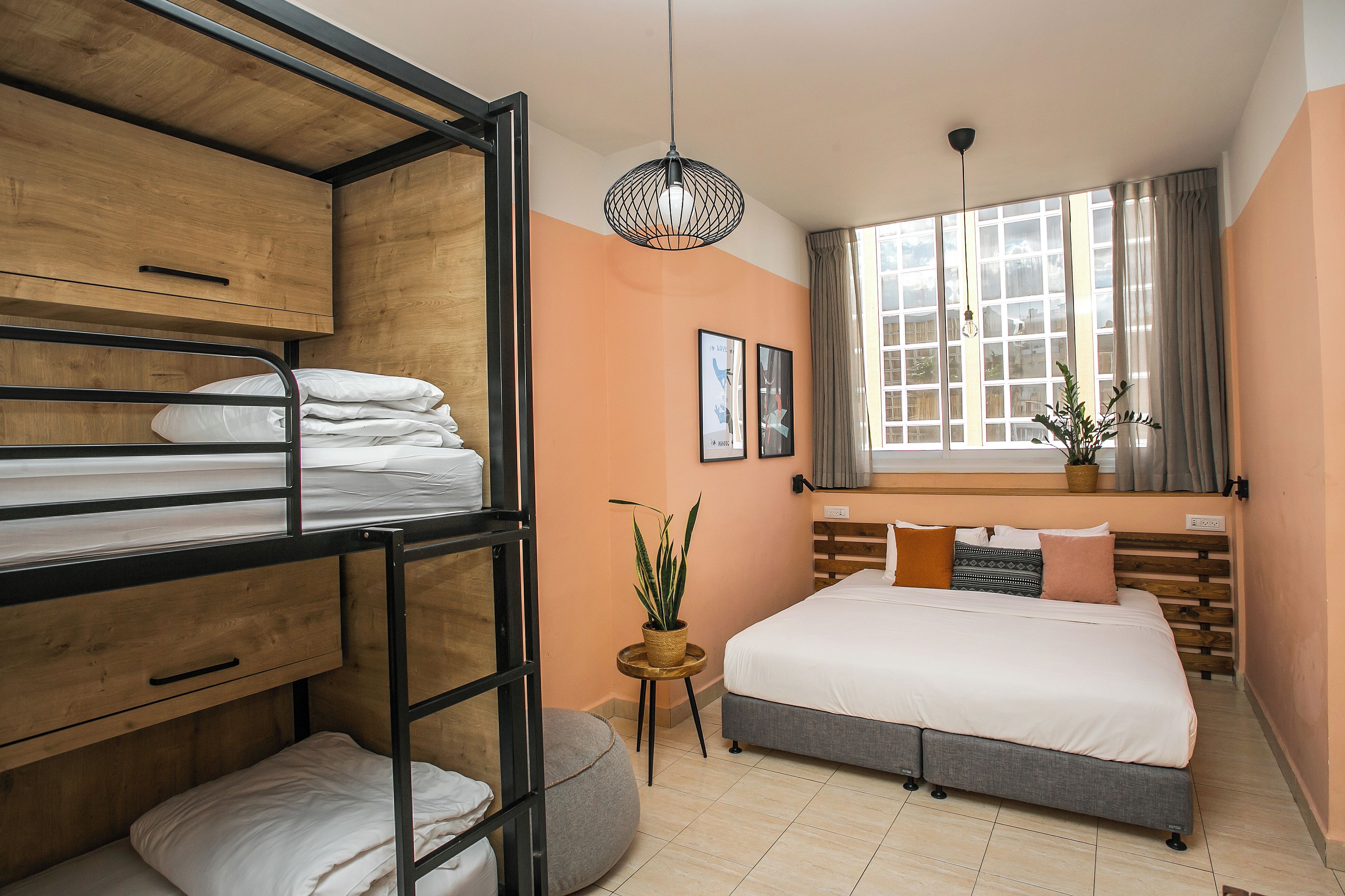 A room with bunk beds, a single bed, a small table with a plant, and a window with curtains.