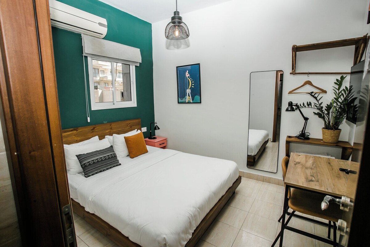 Une chambre à coucher avec un lit, une table de chevet, une lampe suspendue, un miroir et une plante en pot.