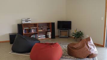 Una sala de estar con una estantería, un televisor de pantalla plana y dos sillones de tular.
