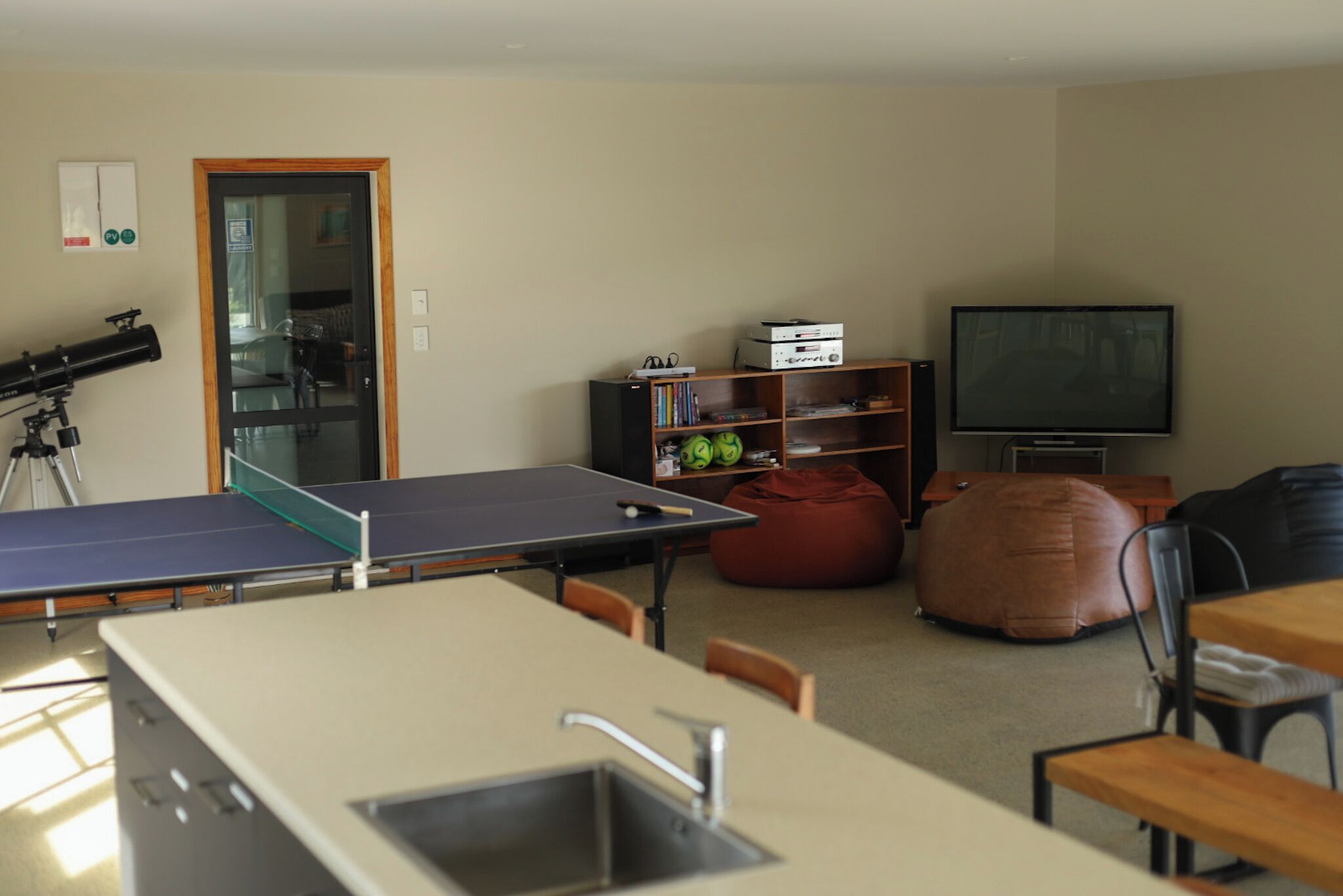 Quarto com mesa de pingue-pongue, cozinha compacta, televisão e poltrona de poliespuma.