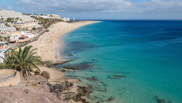 Una playa costera con aguas transparentes, una orilla arenosa y edificios a lo largo de la costa.
